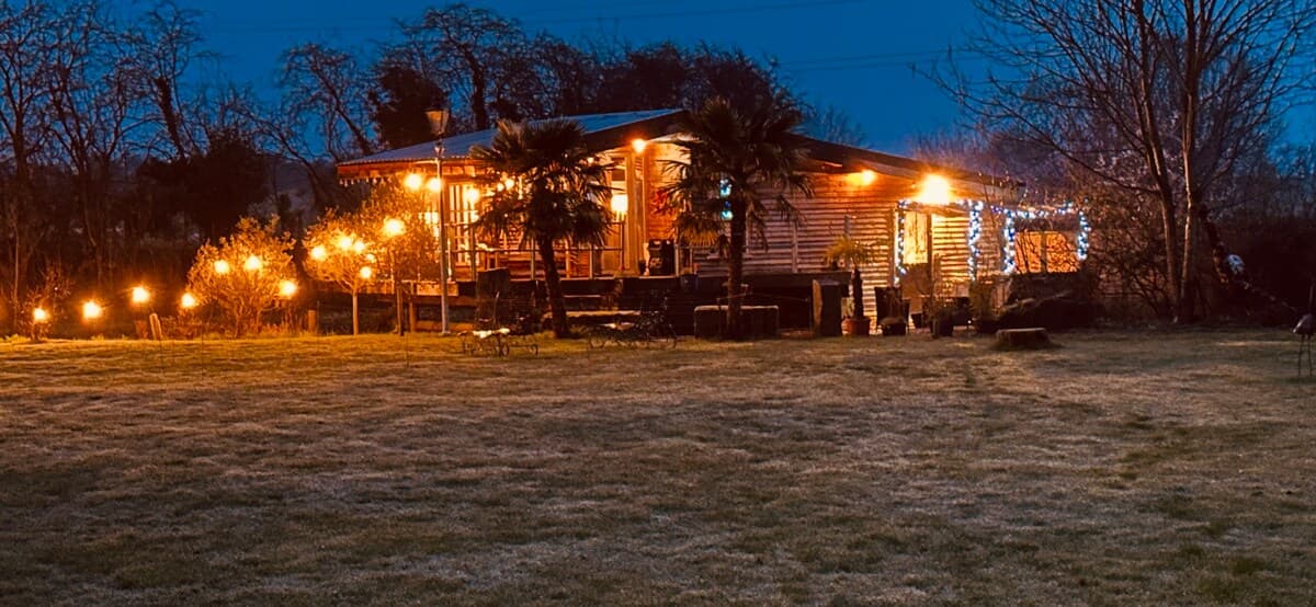 Charming log cabin illuminated at dusk, nestled in countryside with ambient lighting and palm trees creating a warm, inviting retreat.