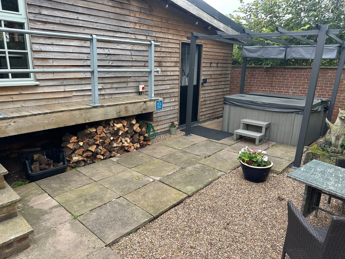 Enclosed patio area with wood burner storage, hot tub with pergola shelter, and flagstone terrace perfect for al fresco relaxation.
